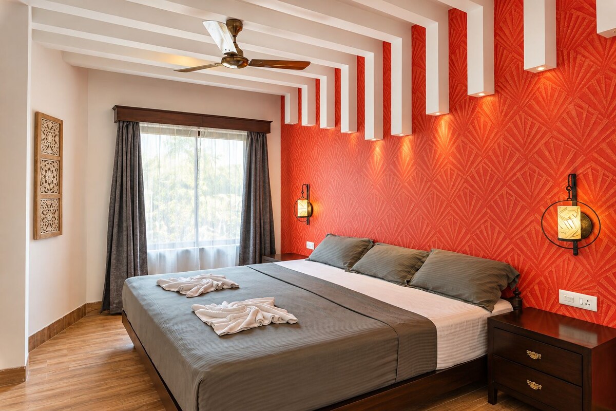 A hotel room with a bed, a ceiling fan, a window with curtains, and a wall with patterned wallpaper.
