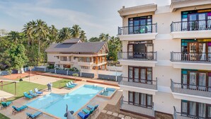 A hotel with a swimming pool, multiple balconies, and a view of palm trees. - Villa Calangute Phase 17 (Calangute)