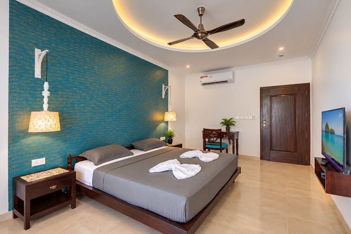 A hotel room with a bed, a ceiling fan, a TV, and a desk with a chair.