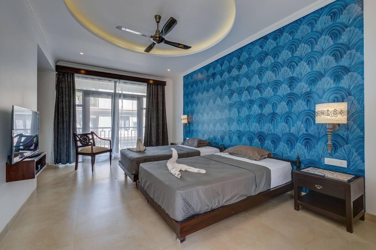 A hotel room with two beds, a ceiling fan, a TV, a chair, and a large window with curtains.