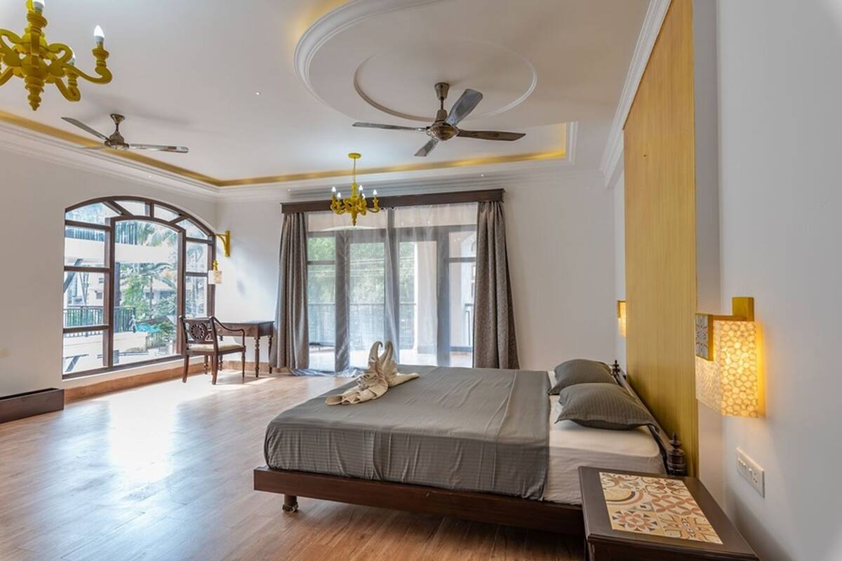 A bedroom with a bed, a chandelier, ceiling fans, and a view through large windows.