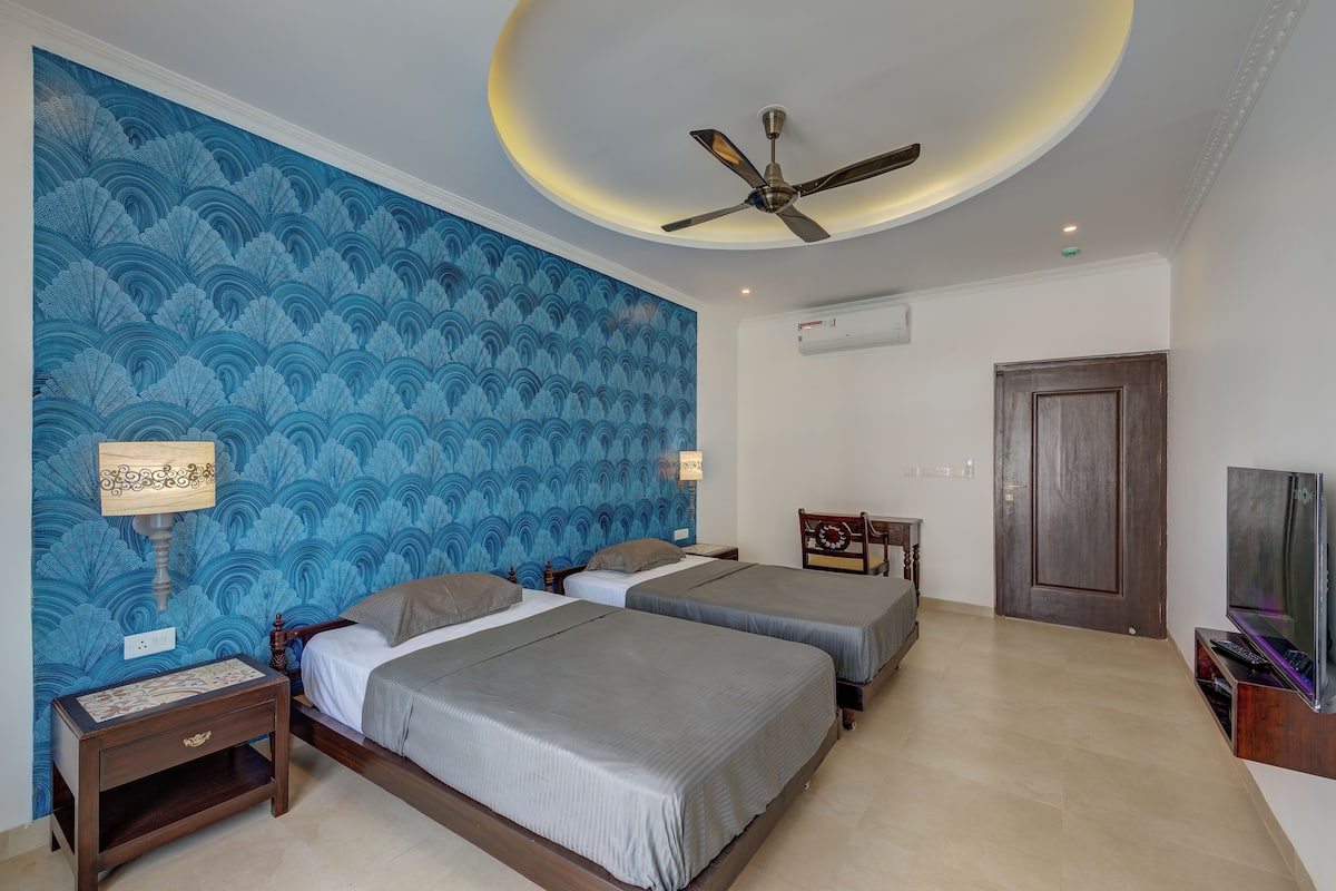 A hotel room with two beds, a ceiling fan, a TV, and a wall with a blue wave pattern.