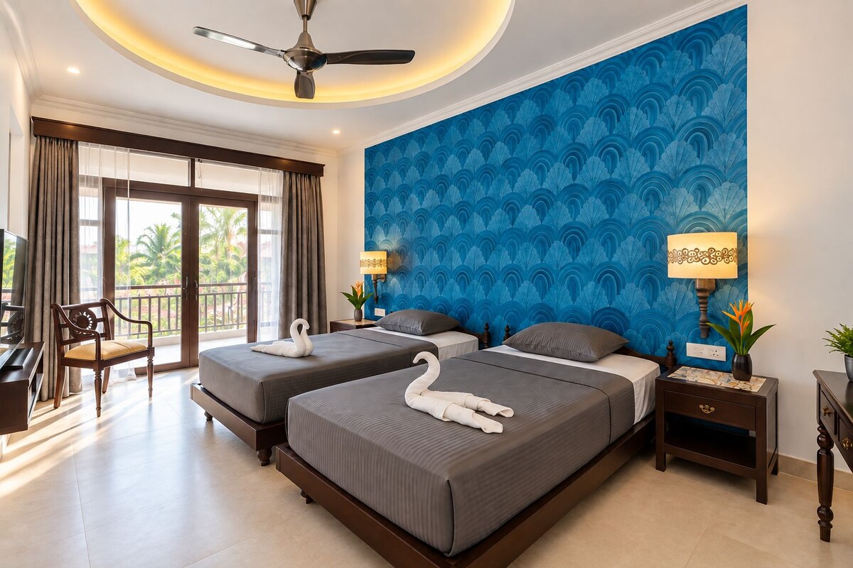 A hotel room with two beds, a ceiling fan, a balcony with curtains, and a blue patterned wall.