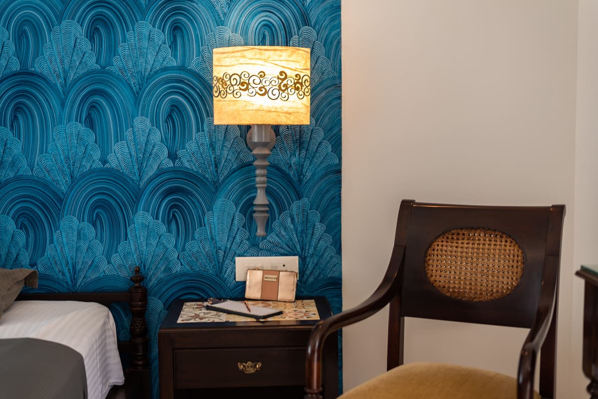 A room with a bed, a nightstand with a lamp, a chair, and a wall with a blue pattern.
