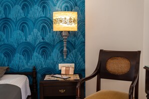 A room with a bed, a nightstand with a lamp, a chair, and a wall with a blue pattern.