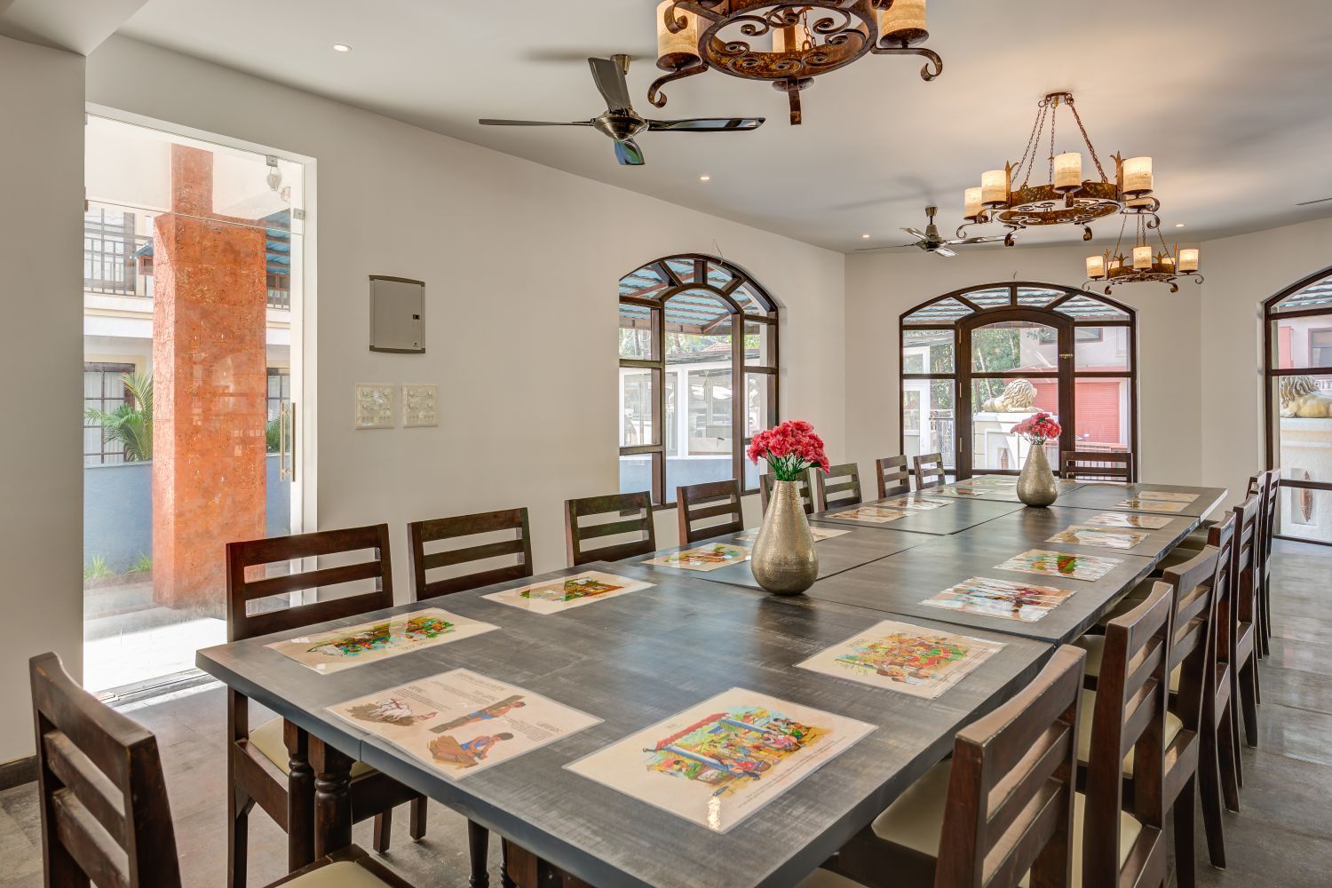A long dining table with chairs, a vase with flowers, and artwork on placemats.