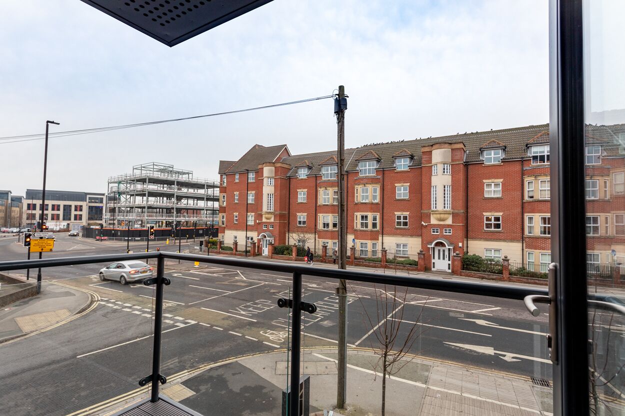 A view from a balcony overlooking a street with a red brick building, a bus stop, and a pedestrian crossing.