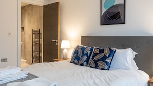 A hotel room with a bed, a nightstand, a lamp, a towel rack, and a shower area. - Modern & Stylish 2 Bed York Apartment (York)