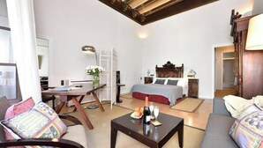 A hotel room with a bed, a desk, a chair, a sofa, and a table with a bottle and glasses.