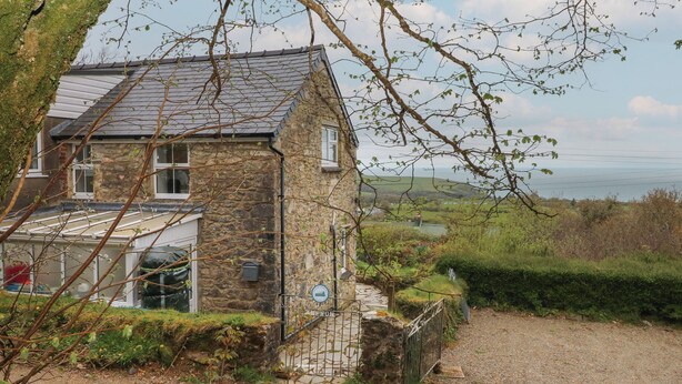 A stone house with a sloped roof, a gravel driveway, and a view of the sea. - Arfron (Newport)