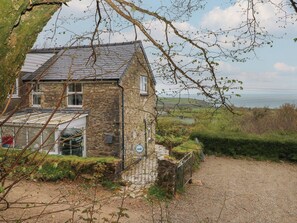 A stone house with a sloped roof, a gravel driveway, and a view of the sea. - Arfron (Newport)