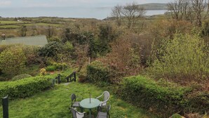 A garden with a table and chairs, surrounded by greenery and a view of the sea. - Arfron (Newport)