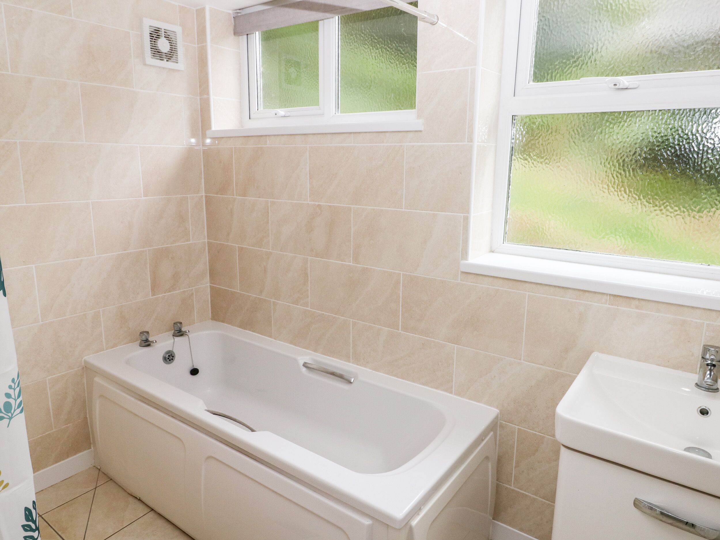 A bathroom with a bathtub, a sink, and a window with a view of greenery.