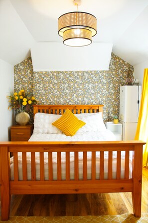 A bedroom with a wooden bed, a nightstand, a vase with flowers, and a floral-patterned wallpaper. - House Near Cardiff City Centre (Cardiff)
