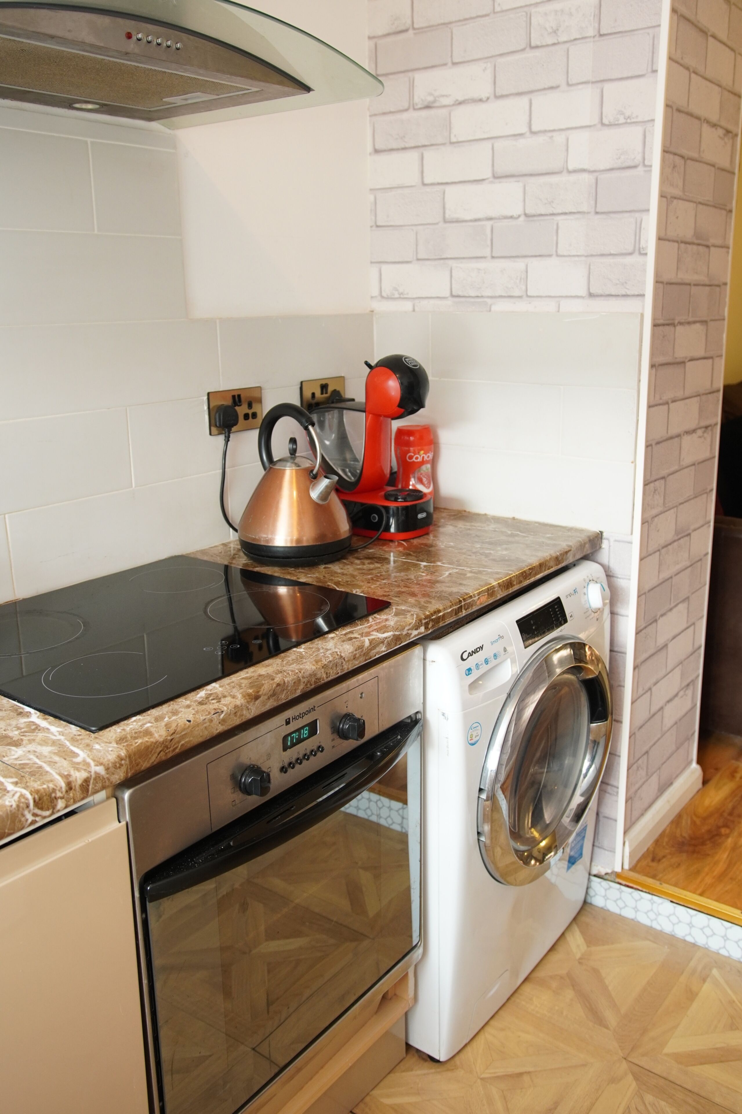 A compact kitchen with a built-in oven, a washing machine, and a kettle on the countertop.
