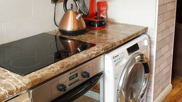 A compact kitchen with a built-in oven, a washing machine, and a kettle on the countertop.