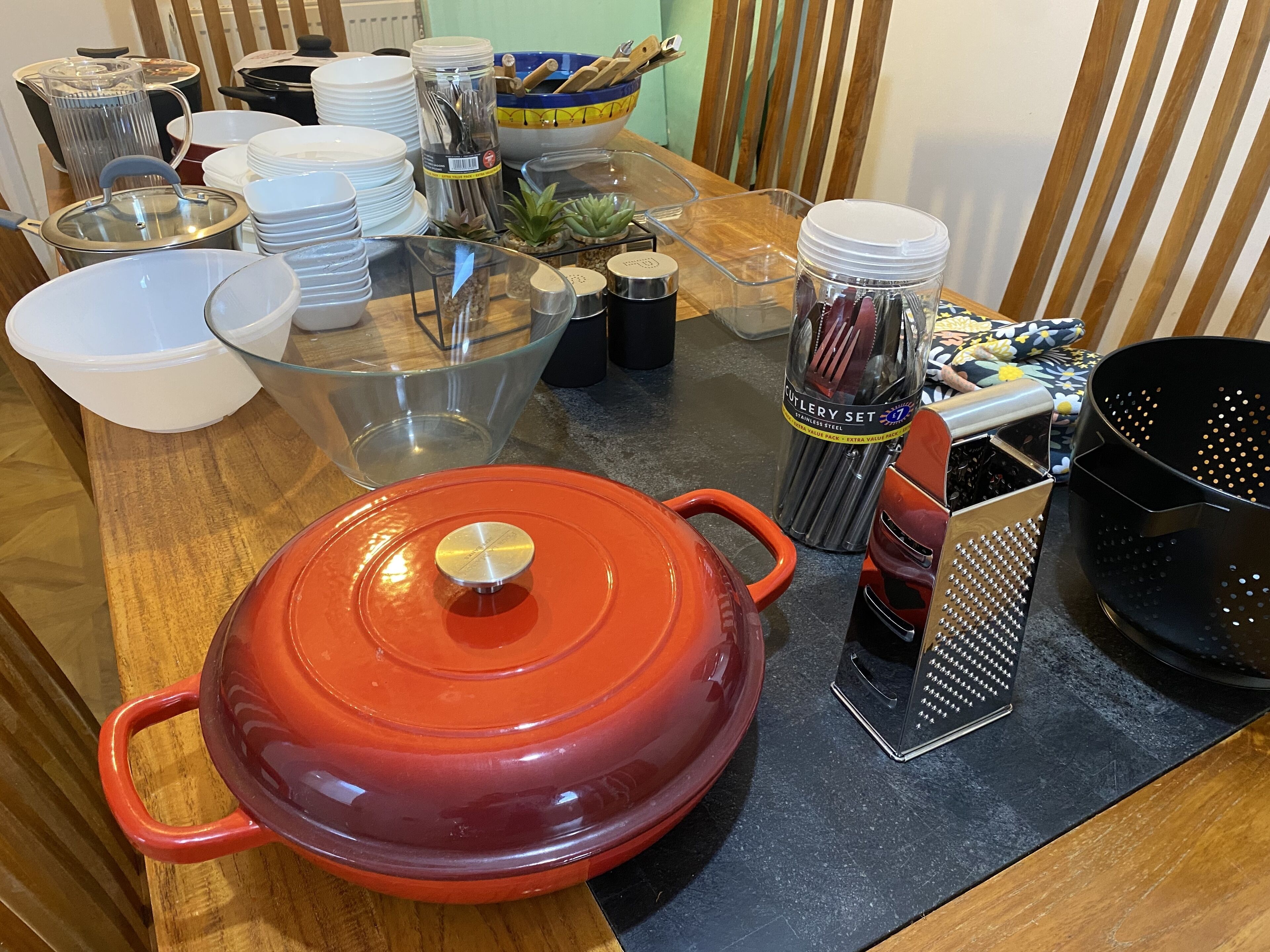 A kitchen counter with a red pot, a colander, a grater, and various kitchen utensils.