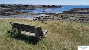 A bench overlooking a rocky shoreline with boats in the water. - Roulotte Karantez Hébergement Insolite à 800 m des Plages Séjour 100 % Cocooning (Porspoder)