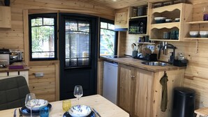 A compact kitchen with wooden cabinets, a built-in dishwasher, and a dining area with a table set for two. - Roulotte Karantez Hébergement Insolite à 800 m des Plages Séjour 100 % Cocooning (Porspoder)