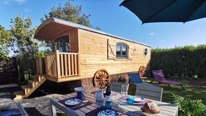 A wooden cabin with a deck, a table set for dining, and a large umbrella. - Roulotte Karantez Hébergement Insolite à 800 m des Plages Séjour 100 % Cocooning (Porspoder)