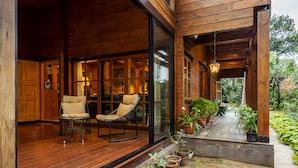 A wooden exterior with a covered porch, two cushioned chairs, and potted plants.