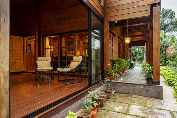 A wooden exterior with a covered porch, two cushioned chairs, and potted plants. - ama Stays & Trails The Malabar Villa Heliconia, Kozhikode (Kozhikode)
