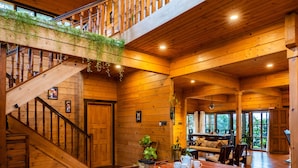 A spacious wooden interior with a central dining area, a staircase, and a balcony with wooden railings.