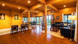 A spacious wooden cabin interior with a dining area, seating, and a large window providing a view of the outdoors.
