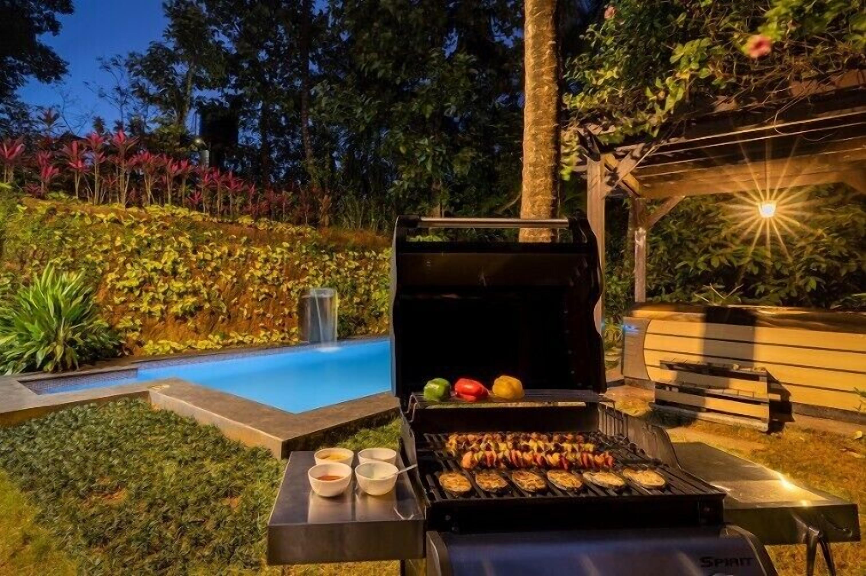 An outdoor barbecue area with a grill, a pool, and a wooden pergola.