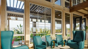 Une pièce spacieuse avec de grandes fenêtres, des fauteuils de couleur turquoise et une petite table sur laquelle est posé un vase.