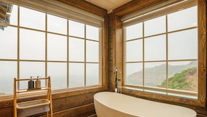 Une salle de bain avec une baignoire sur pieds, des murs en bois et de grandes fenêtres donnant sur un paysage montagneux.