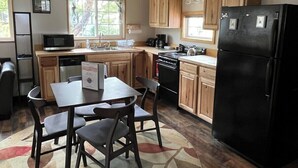 A compact kitchen with wooden cabinets, a black refrigerator, a dining table with chairs, and a microwave. - The Chillton Cozy cabin steps to beach (Cloverdale)