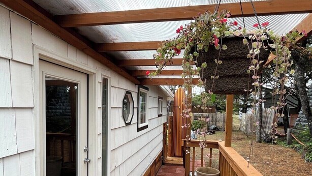 A wooden deck with a pergola, a hanging flower basket, and a door leading to a covered area. - The Chillton Cozy cabin steps to beach (Cloverdale)