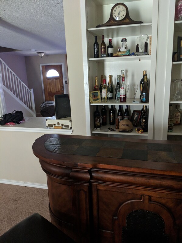 Un intérieur de maison comprenant un comptoir de bar en bois, une horloge et un meuble à vin contenant différentes bouteilles.