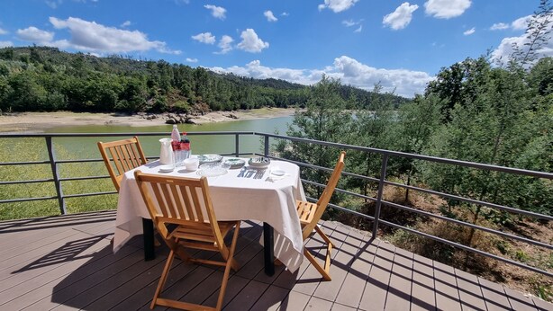 Mesa para dos en una terraza al aire libre con vista a un río y un bosque.