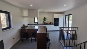 Una cocina moderna con una isla central, taburetes de bar, un refrigerador y un ventanal grande.