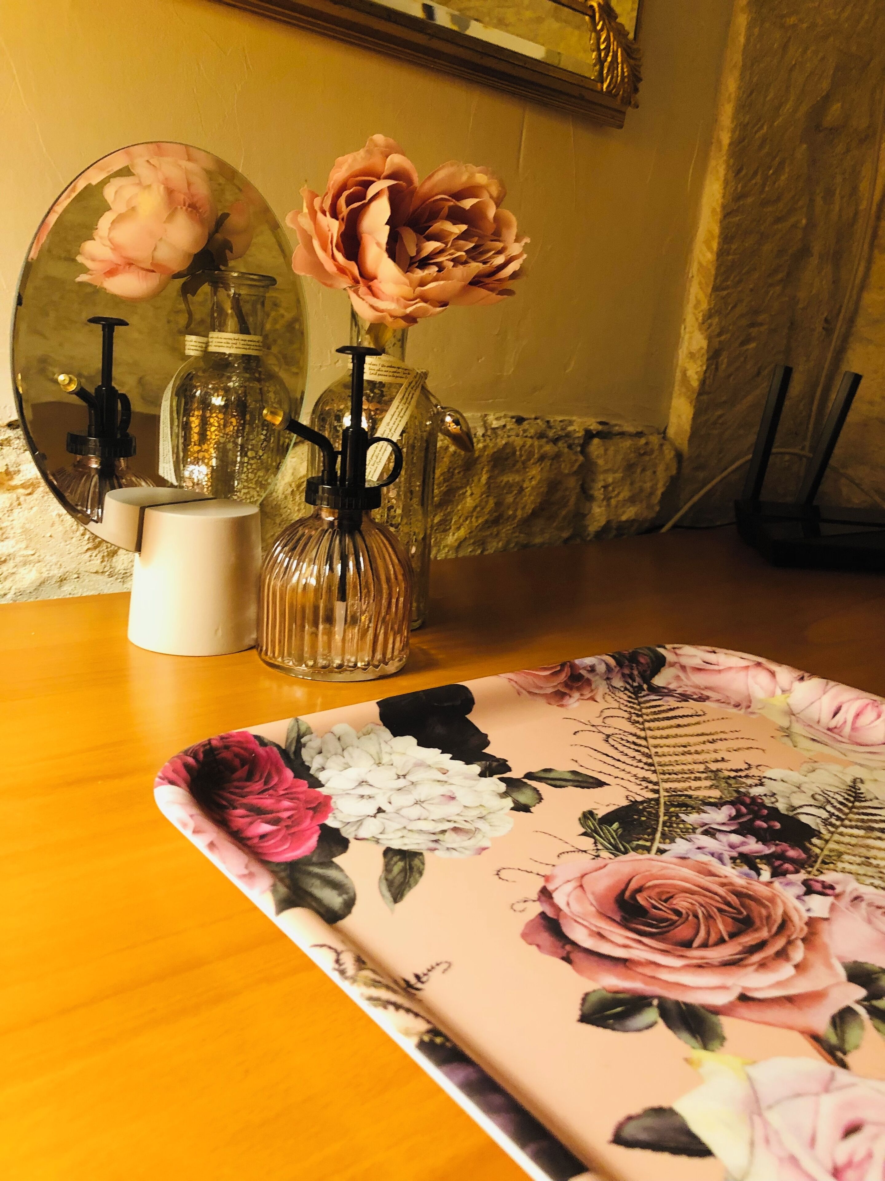 Una mesa con mantel floral, un espejo y botellas de vidrio decorativas con flores.