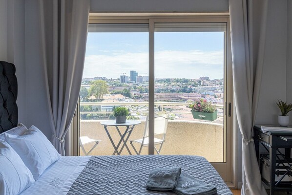 Une chambre avec une grande fenêtre, un lit, une petite table et une chaise.