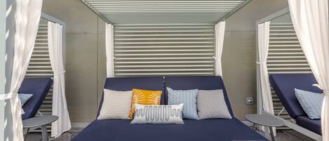 A room with a bed, two lounge chairs, a small table, and a ceiling fan.