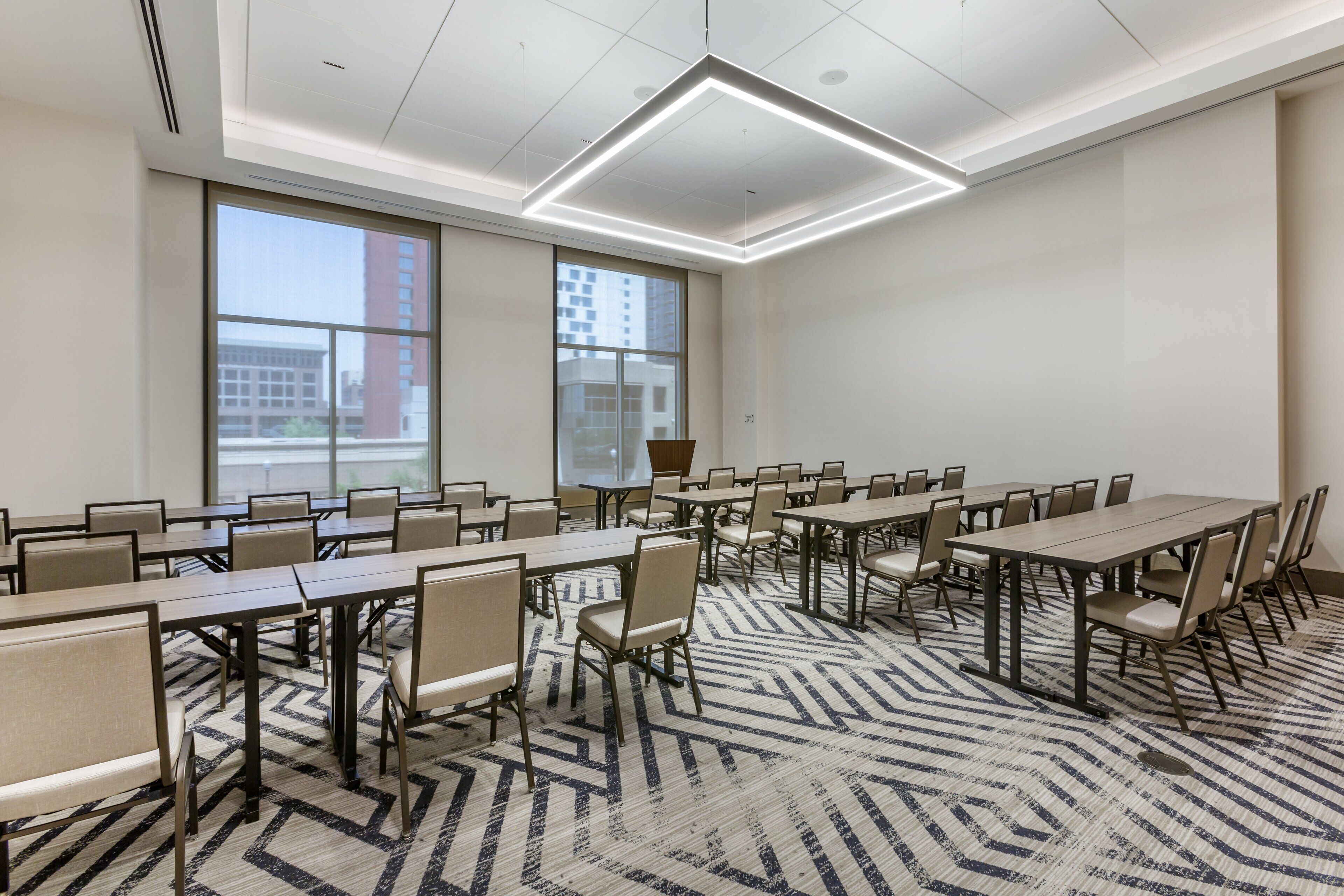 A conference room with multiple tables and chairs, large windows, and a patterned carpet.