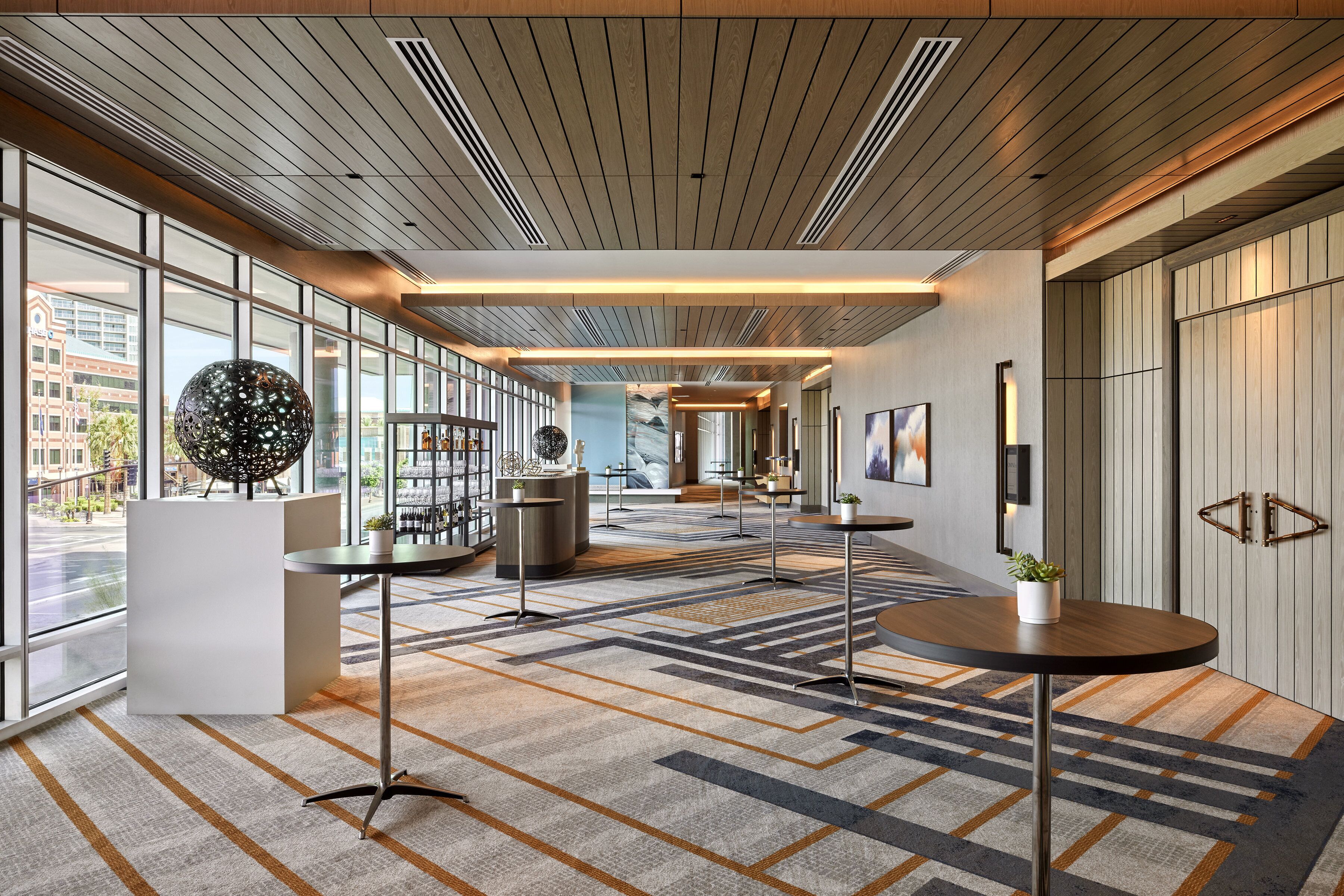 Un hall d’hôtel moderne, doté de grandes fenêtres, d’un tapis à motifs et de mobilier contemporain.