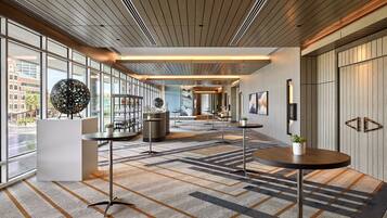 Un hall d’hôtel moderne, doté de grandes fenêtres, d’un tapis à motifs et de mobilier contemporain.