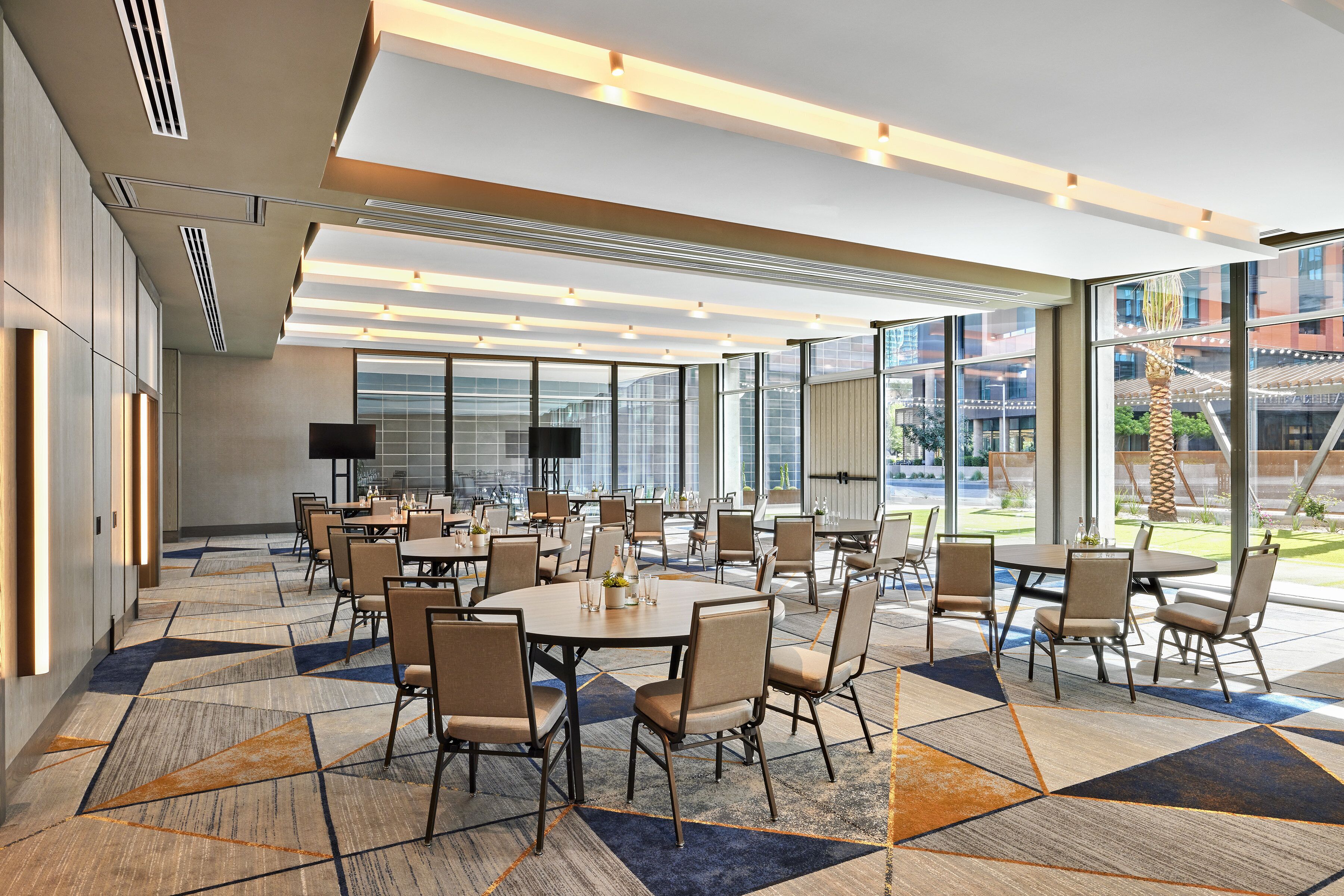 A modern conference room with round tables and chairs, large windows, and a patterned carpet.