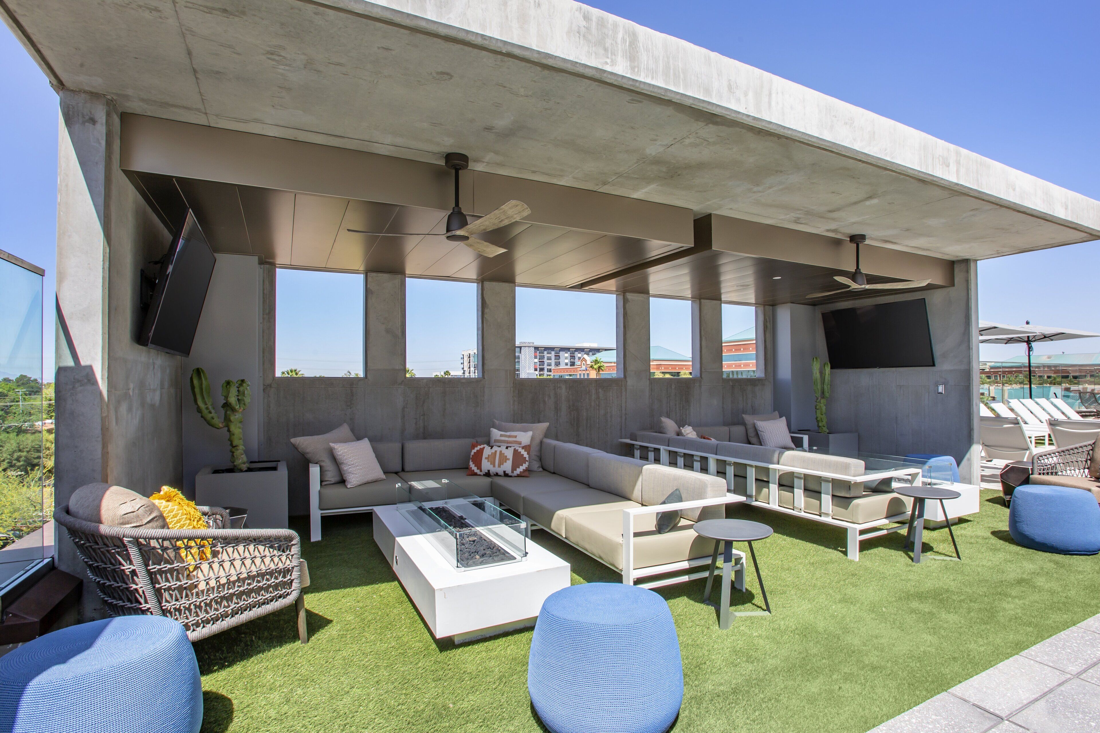 An outdoor patio with a sofa set, a dining table, and a flat-screen TV mounted on a concrete wall.