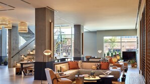 A spacious lobby with a modern sofa, a wooden coffee table, and a seating area with a chair. There is a staircase in the background and a large window providing a view of the outside. - Omni Tempe Hotel at ASU (Tempe)