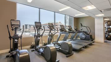 Ein Fitnessstudio mit mehreren Trainingsgeräten, großen Fenstern und Blick auf Gebäude.