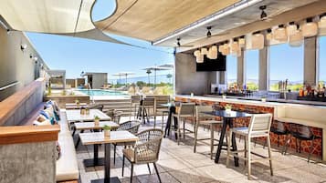 Zona de bar al aire libre con asientos y piscina al fondo.