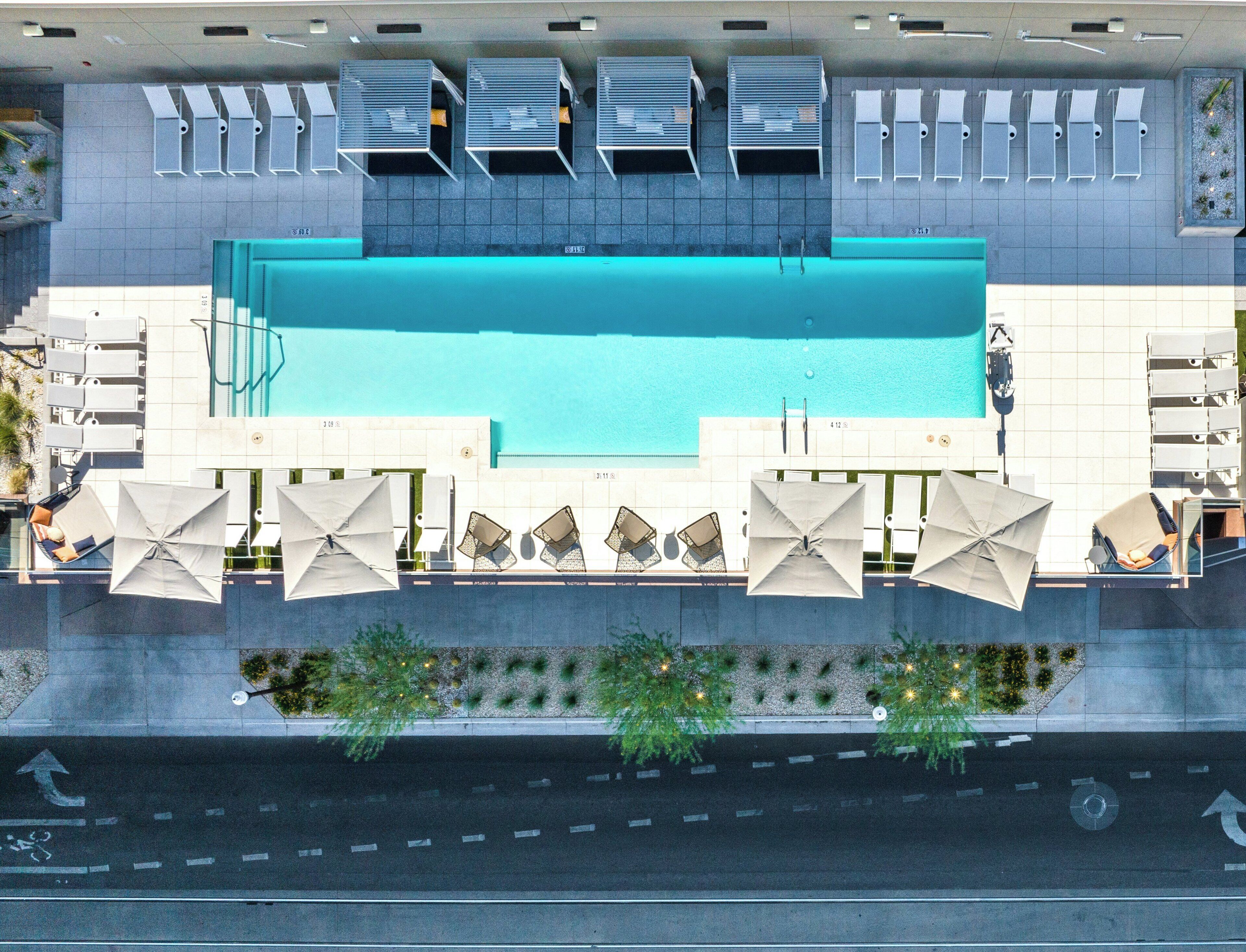 A rooftop swimming pool with sun loungers and umbrellas, surrounded by a modern building with a tiled facade.