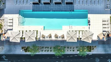 A rooftop swimming pool with sun loungers and umbrellas, surrounded by a modern building with a tiled facade.