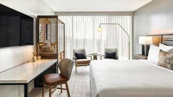 A modern hotel room with a large bed, a desk, a chair, a small table, and a TV.
